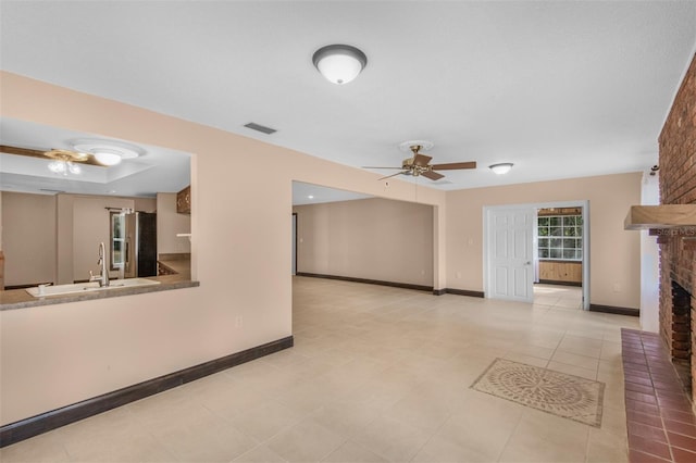 unfurnished living room featuring ceiling fan, a fireplace, light tile patterned floors, and sink