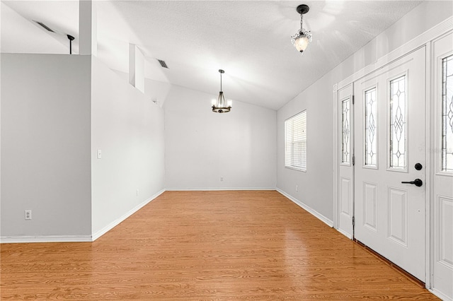 entrance foyer with a textured ceiling, a notable chandelier, lofted ceiling, and light wood-type flooring