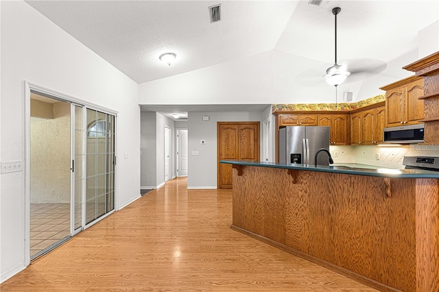 kitchen featuring ceiling fan, kitchen peninsula, light hardwood / wood-style floors, vaulted ceiling, and appliances with stainless steel finishes