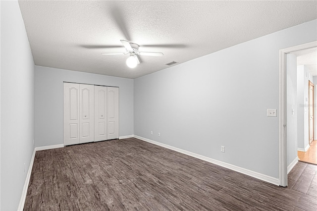 unfurnished bedroom with a textured ceiling, ceiling fan, dark wood-type flooring, and a closet