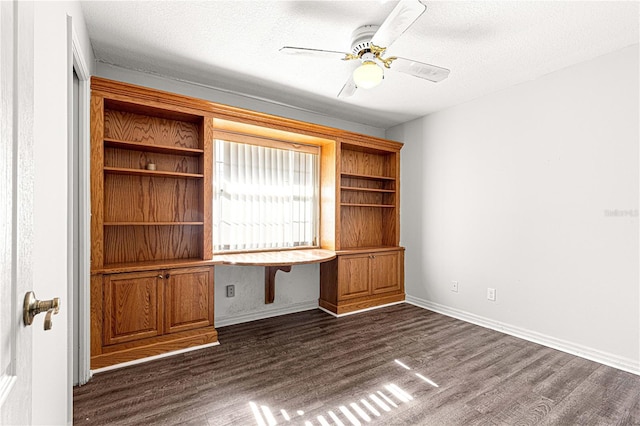 unfurnished office featuring ceiling fan, dark hardwood / wood-style flooring, built in desk, and a textured ceiling