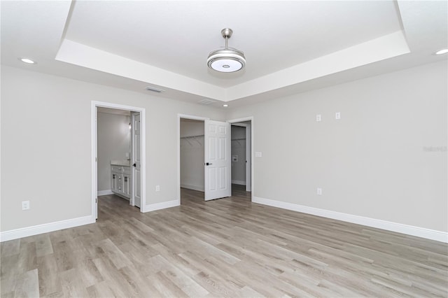 unfurnished bedroom featuring light wood-type flooring, a walk in closet, ensuite bathroom, and a closet