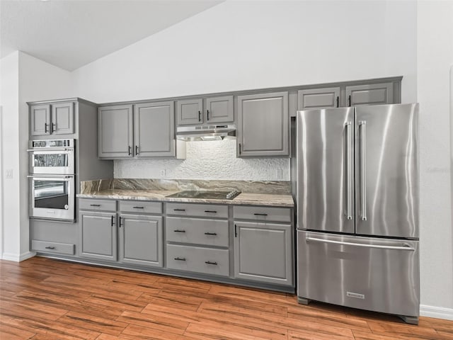 kitchen with gray cabinetry, backsplash, light stone counters, wood-type flooring, and stainless steel appliances