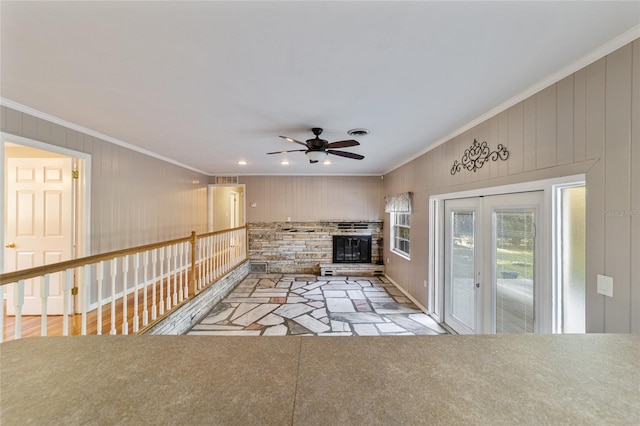 unfurnished living room with ceiling fan, wood walls, and ornamental molding