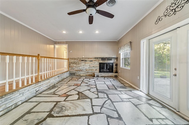 unfurnished living room featuring a stone fireplace, ceiling fan, crown molding, and wood walls