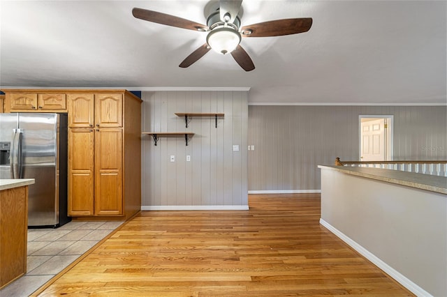 kitchen with stainless steel fridge, ceiling fan, crown molding, wooden walls, and light hardwood / wood-style floors