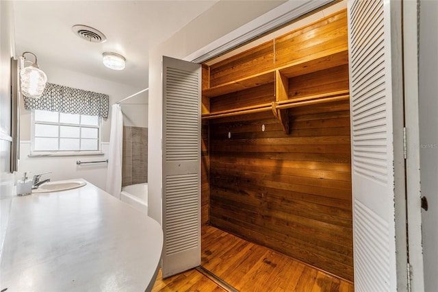 bathroom featuring walk in shower, wood walls, hardwood / wood-style floors, and sink