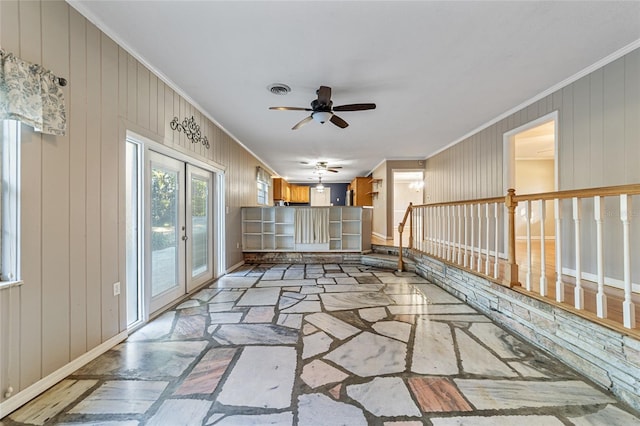 unfurnished living room featuring wooden walls, french doors, ceiling fan, and ornamental molding