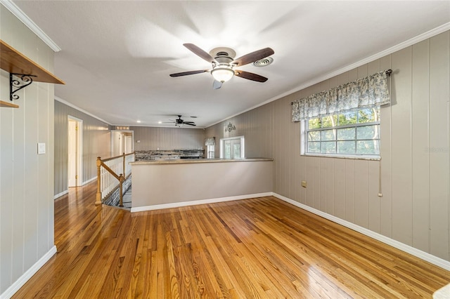 spare room featuring ceiling fan, wood walls, light wood-type flooring, and crown molding