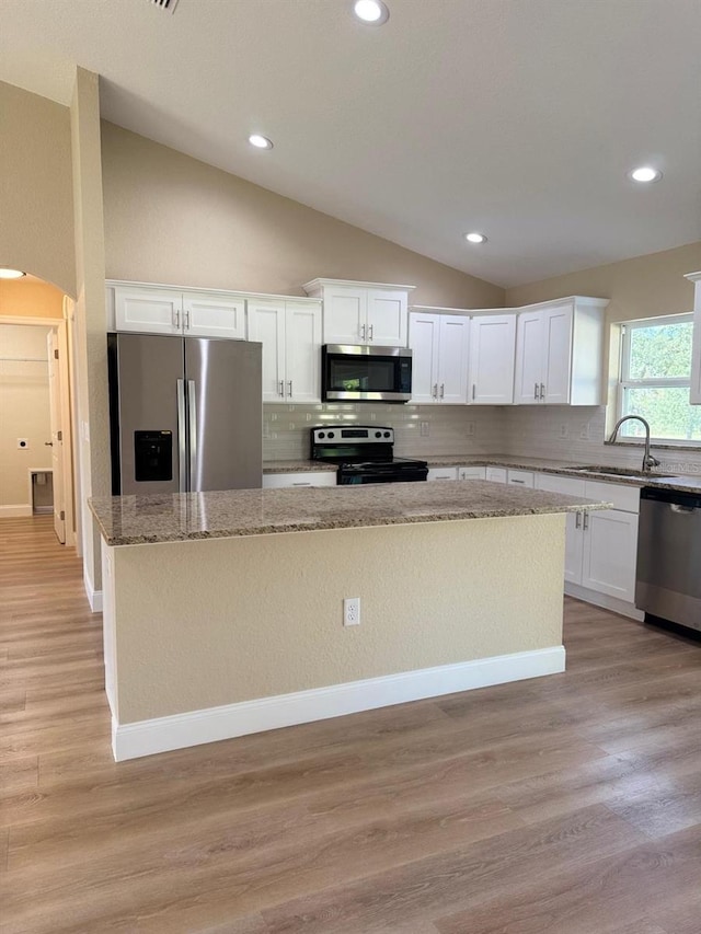 kitchen with light hardwood / wood-style flooring, a kitchen island, lofted ceiling, and appliances with stainless steel finishes