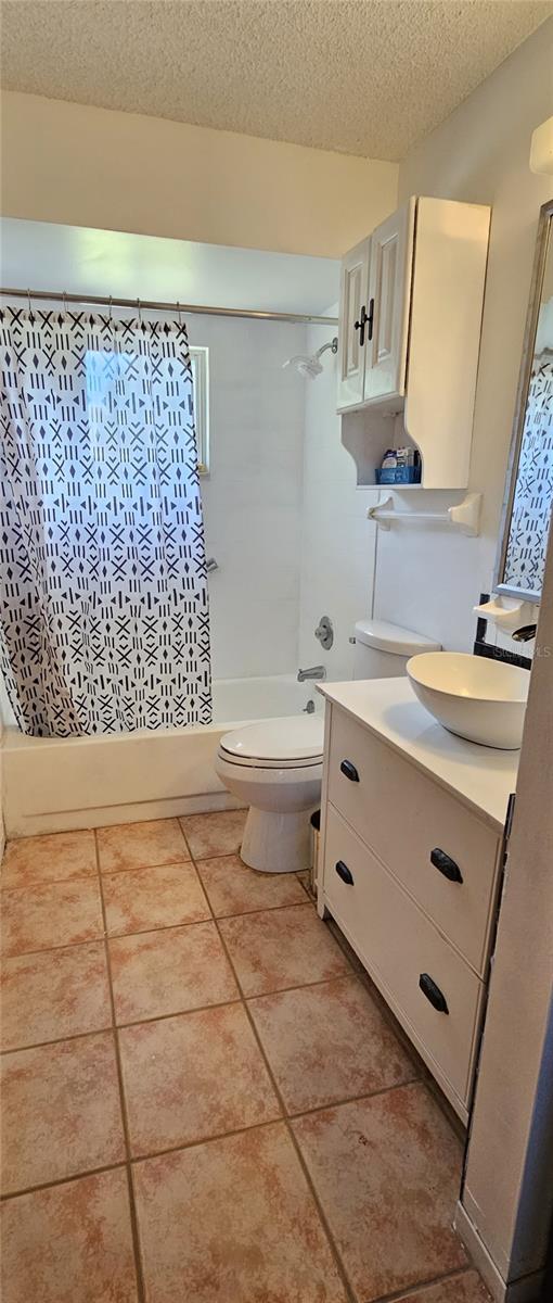 full bathroom featuring shower / bathtub combination with curtain, tile patterned floors, toilet, a textured ceiling, and vanity