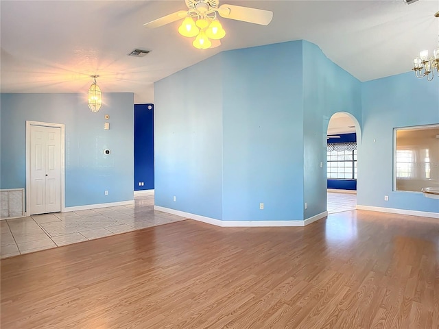 empty room featuring ceiling fan with notable chandelier, lofted ceiling, and light hardwood / wood-style flooring