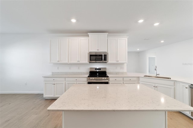 kitchen with light stone countertops, stainless steel appliances, sink, light hardwood / wood-style floors, and a kitchen island