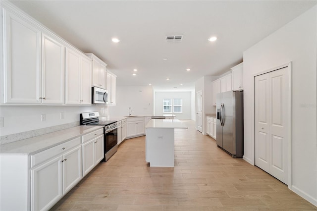 kitchen featuring appliances with stainless steel finishes, light wood-type flooring, a kitchen island, sink, and white cabinetry