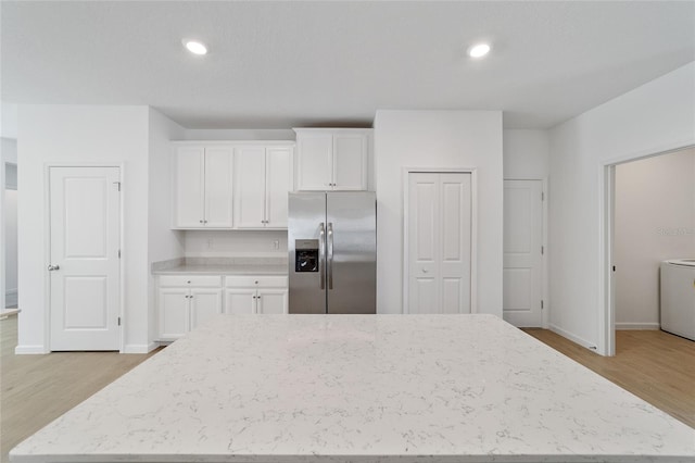 kitchen with white cabinets, stainless steel fridge, light wood-type flooring, and light stone countertops