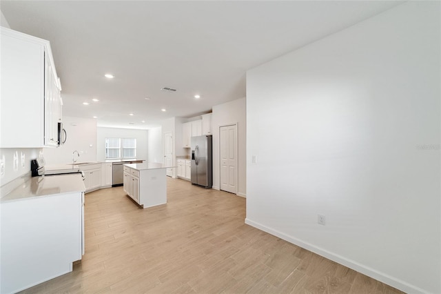 kitchen featuring white cabinetry, sink, stainless steel appliances, a kitchen island, and light wood-type flooring