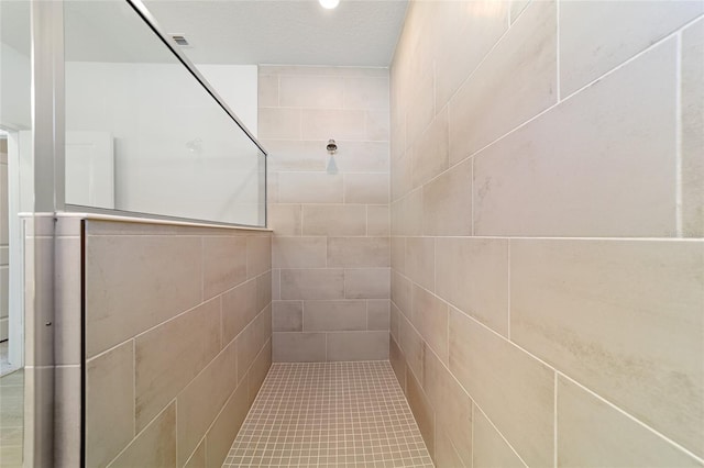 bathroom with a textured ceiling, a tile shower, and tile walls