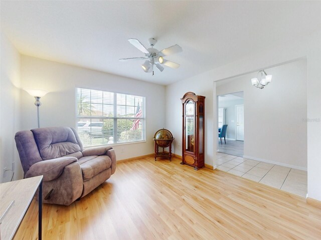 living area featuring ceiling fan with notable chandelier and light wood-type flooring