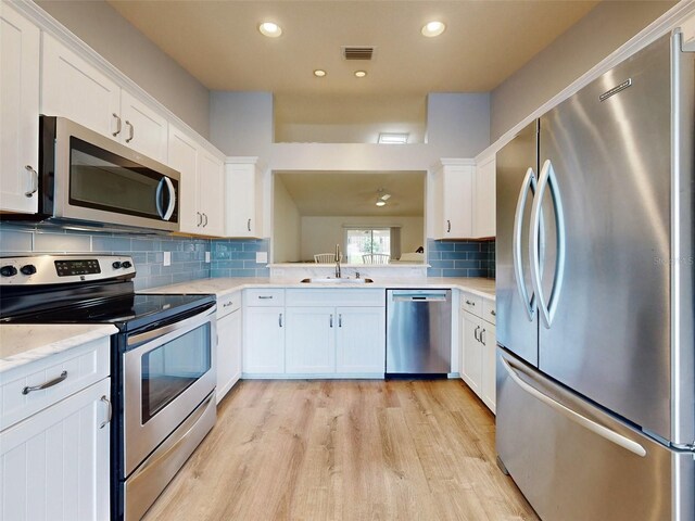 kitchen featuring light wood-type flooring, backsplash, stainless steel appliances, sink, and white cabinets