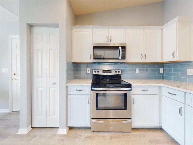 kitchen with white cabinets, appliances with stainless steel finishes, decorative backsplash, and vaulted ceiling