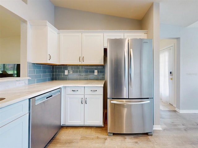 kitchen with appliances with stainless steel finishes, tasteful backsplash, light hardwood / wood-style flooring, white cabinetry, and lofted ceiling