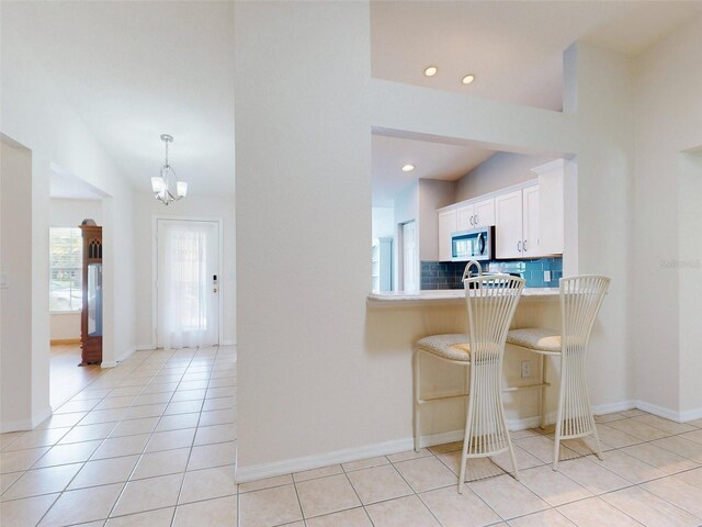 kitchen featuring white cabinets, decorative backsplash, light tile patterned floors, a notable chandelier, and a breakfast bar area