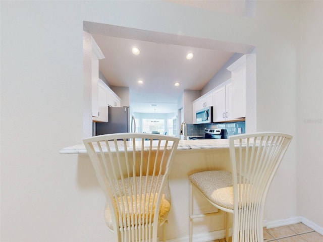 kitchen with sink, backsplash, a kitchen bar, white cabinets, and appliances with stainless steel finishes