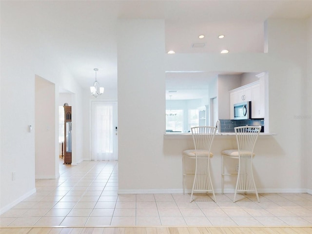 kitchen with a kitchen bar, sink, an inviting chandelier, white cabinetry, and light tile patterned flooring