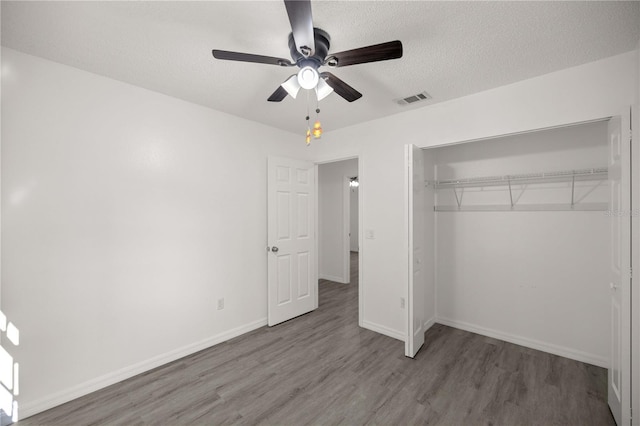 unfurnished bedroom with a textured ceiling, a closet, hardwood / wood-style flooring, and ceiling fan