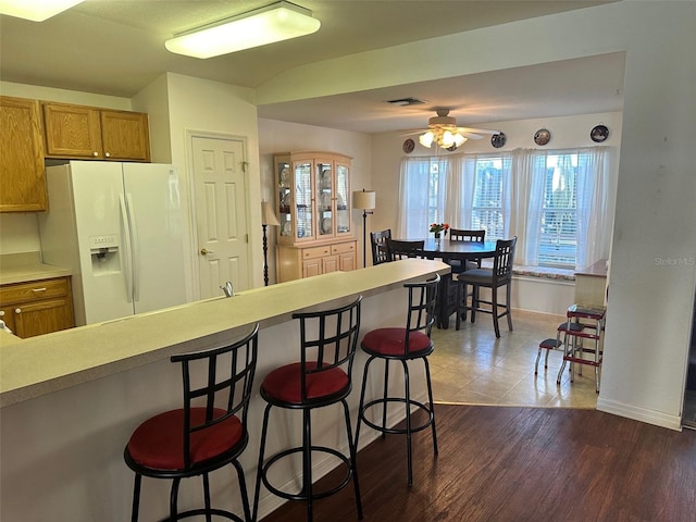 kitchen featuring a kitchen breakfast bar, ceiling fan, dark hardwood / wood-style flooring, and white refrigerator with ice dispenser