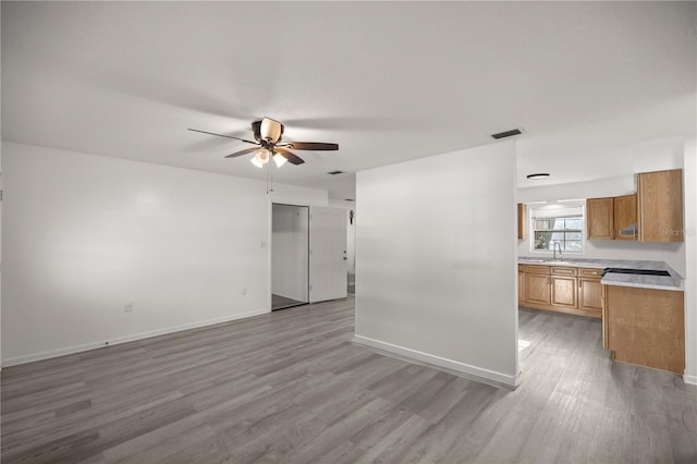 unfurnished living room featuring ceiling fan, sink, and light hardwood / wood-style flooring