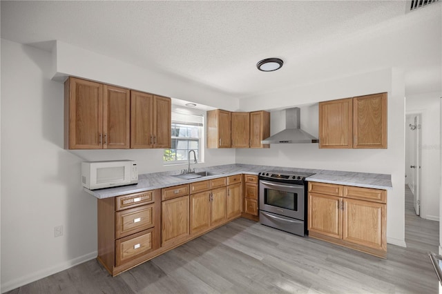 kitchen featuring sink, wall chimney range hood, light hardwood / wood-style flooring, a textured ceiling, and stainless steel electric range