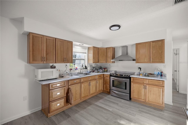 kitchen with sink, wall chimney exhaust hood, stainless steel electric range oven, a textured ceiling, and light hardwood / wood-style floors