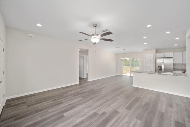 unfurnished living room featuring ceiling fan with notable chandelier and wood-type flooring