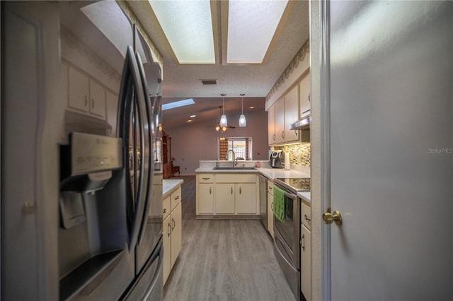 kitchen featuring hanging light fixtures, vaulted ceiling, a textured ceiling, appliances with stainless steel finishes, and kitchen peninsula