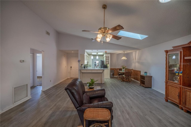 living room with ceiling fan, vaulted ceiling with skylight, and hardwood / wood-style flooring