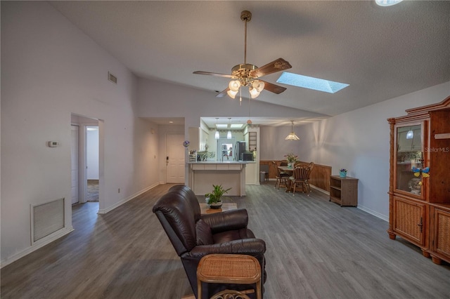 living area featuring hardwood / wood-style flooring, ceiling fan, and lofted ceiling with skylight