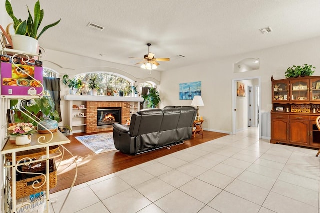 living room with ceiling fan, a fireplace, light hardwood / wood-style floors, and a textured ceiling