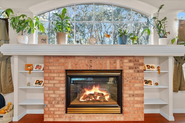 interior details with built in features, wood-type flooring, and a brick fireplace