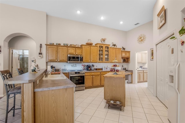 kitchen with sink, kitchen peninsula, a breakfast bar, light tile patterned floors, and appliances with stainless steel finishes