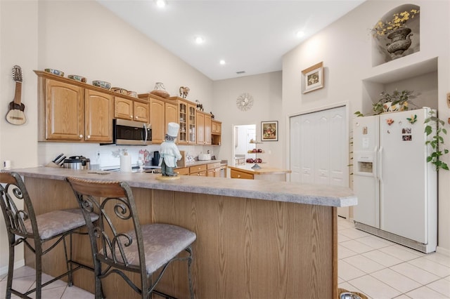 kitchen with kitchen peninsula, a towering ceiling, a breakfast bar, light tile patterned floors, and white fridge with ice dispenser