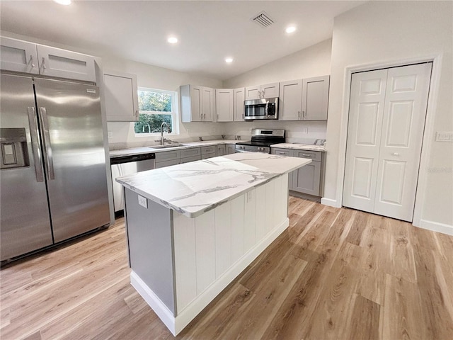 kitchen featuring a center island, sink, stainless steel appliances, light hardwood / wood-style floors, and vaulted ceiling