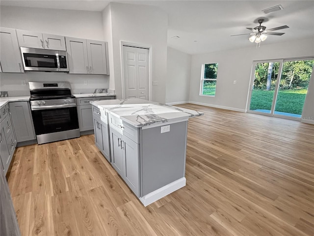 kitchen with light stone countertops, appliances with stainless steel finishes, gray cabinetry, light hardwood / wood-style flooring, and a center island