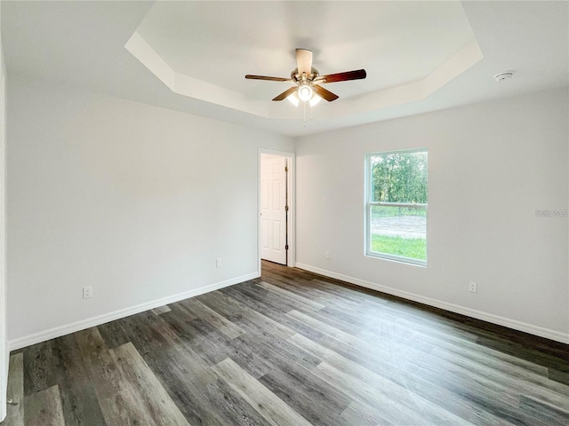 empty room featuring a raised ceiling, ceiling fan, and dark wood-type flooring