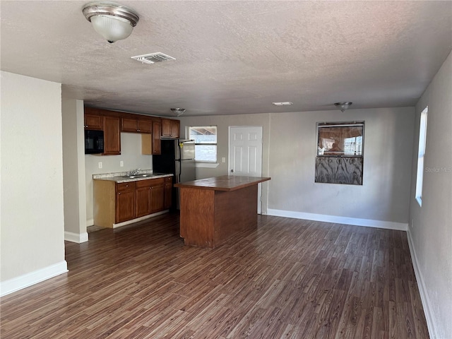 kitchen with stainless steel fridge, a center island, a textured ceiling, and dark wood-type flooring