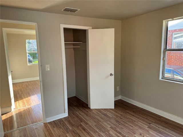 unfurnished bedroom with multiple windows, a closet, and dark wood-type flooring