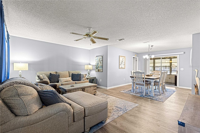 living room featuring ceiling fan with notable chandelier, light hardwood / wood-style floors, and a textured ceiling