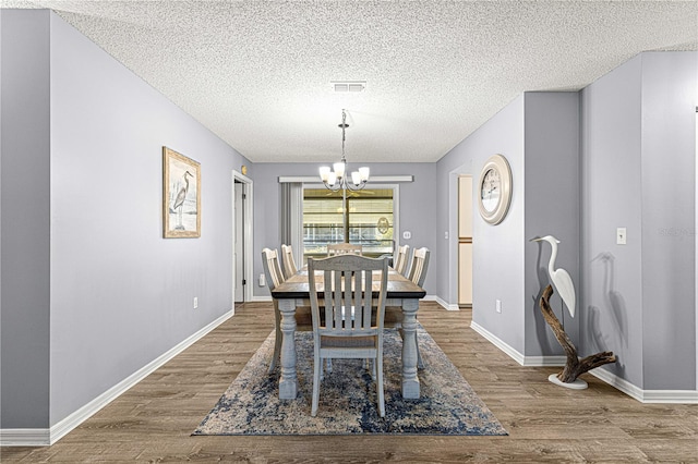 dining space with wood-type flooring, a textured ceiling, and a chandelier