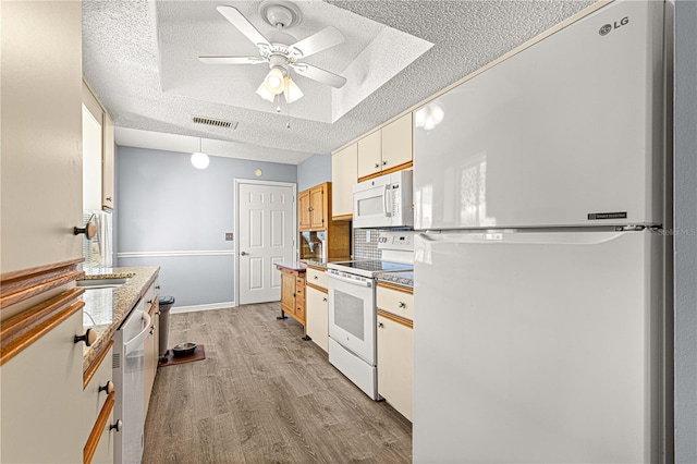 kitchen featuring a raised ceiling, white appliances, a textured ceiling, and light wood-type flooring