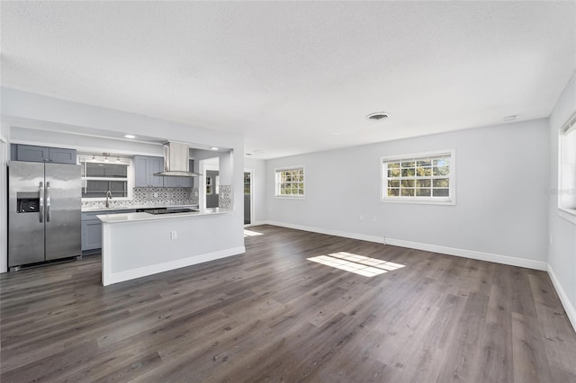 kitchen with gray cabinetry, wall chimney range hood, dark hardwood / wood-style floors, decorative backsplash, and stainless steel fridge with ice dispenser